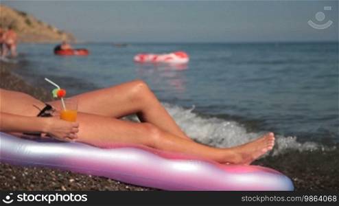 Woman in bikini sunbathing at the beach and holding a cocktail