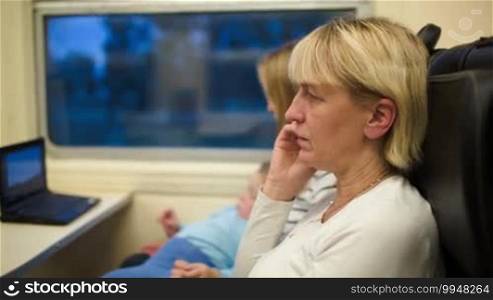 Woman in the train talking on the phone. Mother with son watching a movie in the background