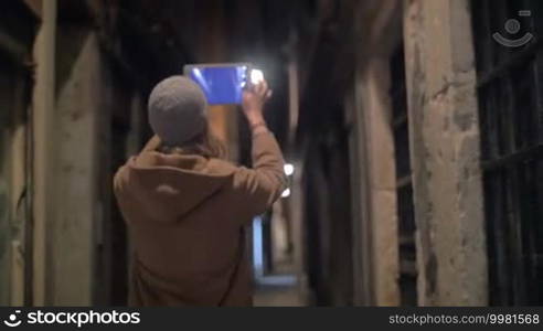 Woman is walking along the narrow street of an old town and taking photos with her tablet PC. Camera is following her.