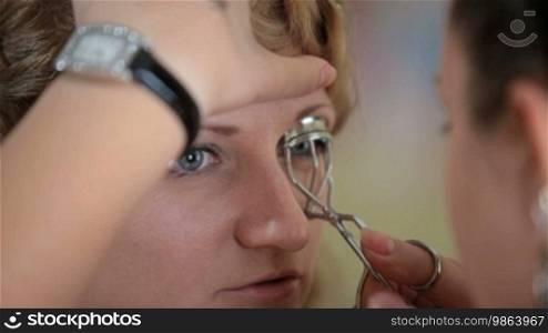 Woman making curled eyelashes using a curling cosmetic tool