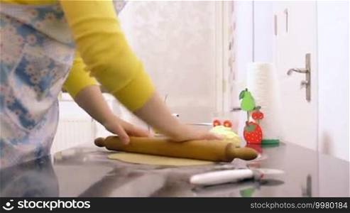 Woman making dough with a rolling pin in the kitchen.
