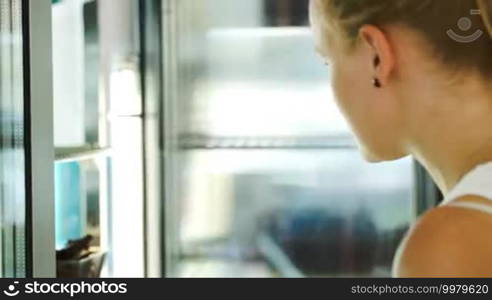 Woman opening fridge at the shop and taking small chocolate cake