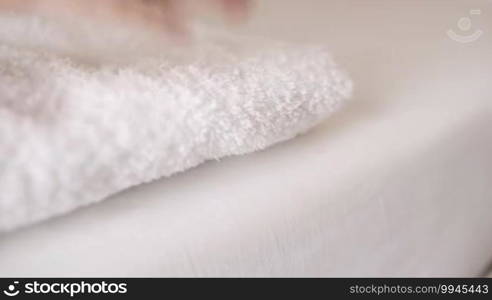 Woman placing a clean fresh white towel on a bed and then smoothing it with her hands