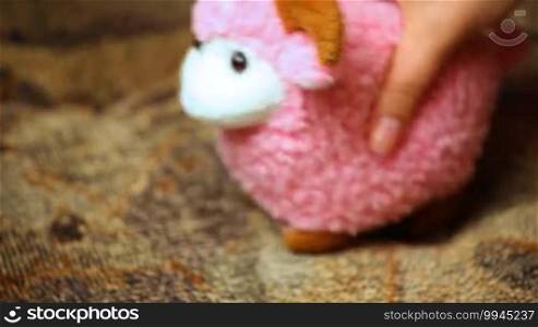 Woman's hand playing toy pink sheep on couch closeup