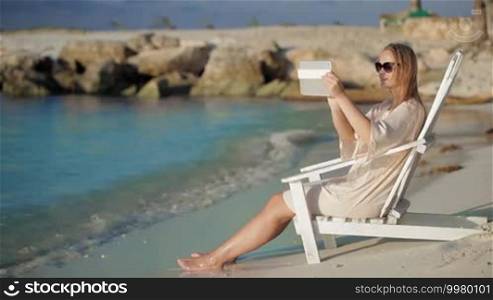 Woman sitting in chaise longue near the sea and taking pictures using tablet computer