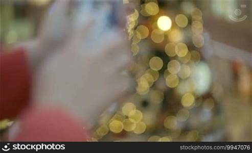 Woman taking pictures of beautiful Christmas tree in shopping center. Zooming in on the object during the process.