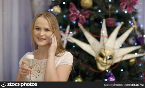 Woman talking on the phone during Christmas celebration and drinking champagne.