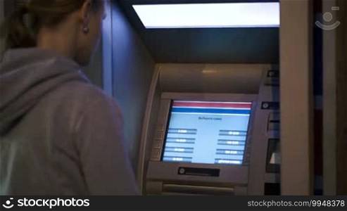 Woman using outdoor ATM in the evening to get cash or to make transaction