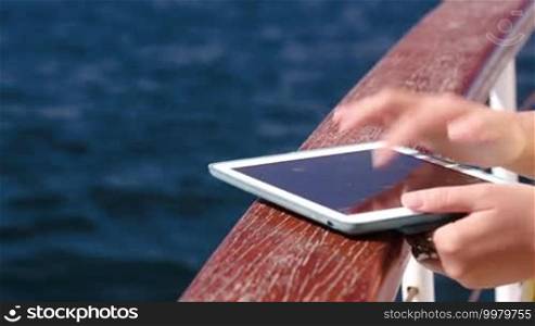Woman using tablet computer holding it on rail of boat or ship. Sea travel with pad