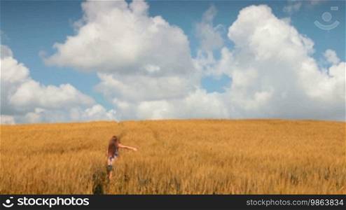 Woman walks on a field of wheat against a blue sky