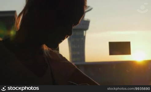 Woman with pen using smart watch while sitting by the window at the airport terminal at golden sunset