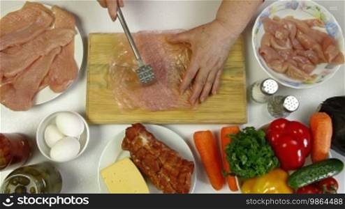 Women's hands cooking chicken breast. Tenderizing, salt, pepper. Top view