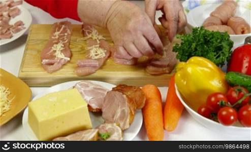 Women's hands cooking rolls of chicken breast, add bacon and cheese.