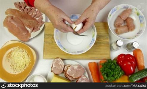 Women's hands cooking rolls of chicken breast, whisking eggs for frying
