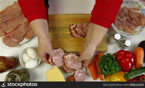 Women's hands slicing pork bacon, an ingredient for cooking chicken roll. Top view