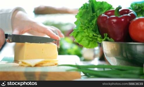 Women's hands slicing the cheese on the kitchen table