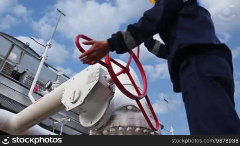 Worker closes ball valve on cooling installations at gas compressor station, against background of cloudy sky, closeup