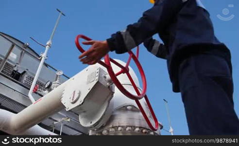 Worker closes ball valve on cooling installations at gas compressor station, against background of blue sky, closeup