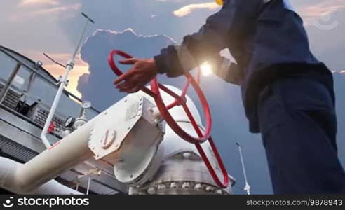 Worker closes ball valve on cooling installations at gas compressor station, against background of sunset, closeup