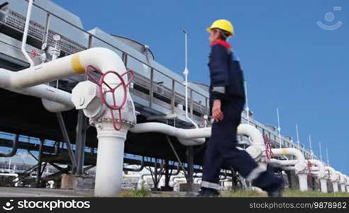 Worker closes ball valve on cooling installations at gas compressor station, against background of blue sky