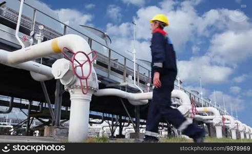 Worker closes ball valve on cooling installations at gas compressor station, against background of cloudy sky