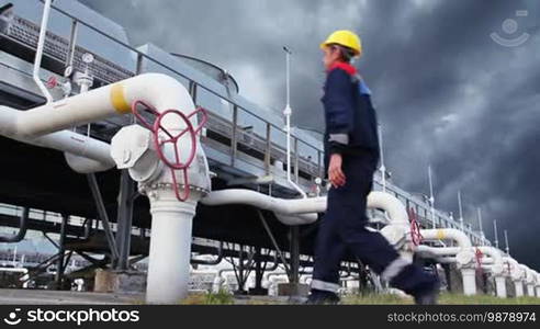 Worker closes ball valve on cooling installations at gas compressor station, against background of thunderstorm sky