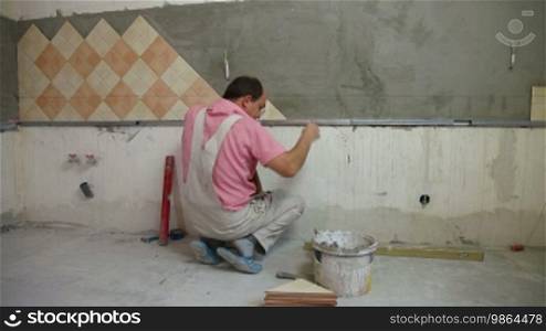 Worker installing tiles on a kitchen wall, wide angle