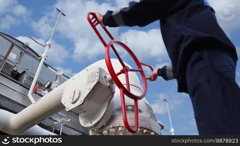 Worker opens ball valve on cooling installations at gas compressor station, against background of cloudy sky, closeup