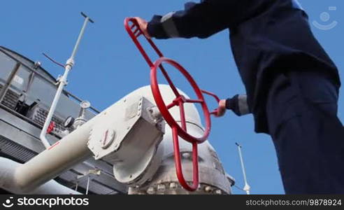 Worker opens ball valve on cooling installations at gas compressor station, against background of blue sky, closeup