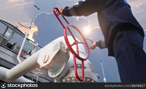 Worker opens ball valve on cooling installations at gas compressor station, against background of sunset, closeup