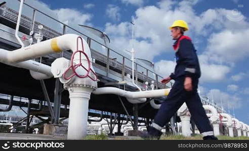 Worker opens ball valve on cooling installations at gas compressor station, against background of cloudy sky