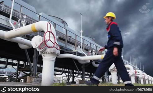 Worker opens ball valve on cooling installations at gas compressor station, against background of thunderstorm sky