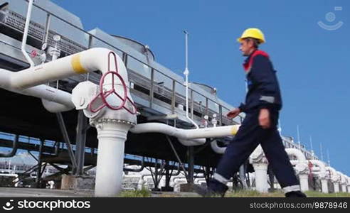 Worker opens ball valve on cooling installations at gas compressor station, against background blue sky