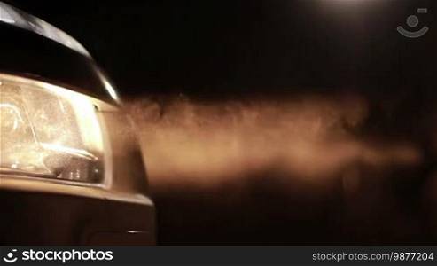 Yellow car headlights in clouds of dust. Bright headlights of car driving on rural dirt road in night time. Closeup.