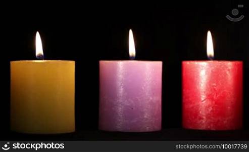 Yellow, purple, and red candles isolated on black. Holiday background with copyspace for text.