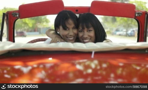 Young adult brunette twin women driving old convertible red car and looking over shoulders