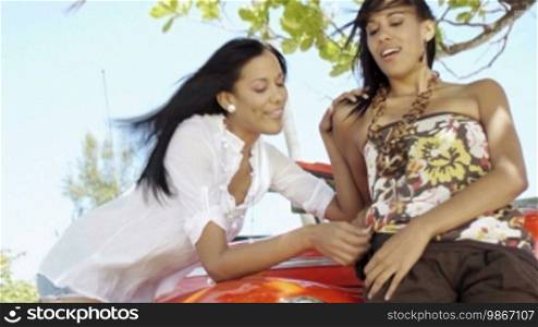 Young adult brunette twin women leaning on convertible red car and smiling