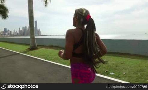 Young African American woman running and exercising early morning in the city, training along the Cinta Costera in Panama, with skyline in background. Slow motion 120p, steadicam shot
