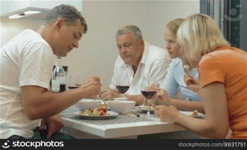 Young and senior people having a meal and clanging glasses with red wine during a home family dinner