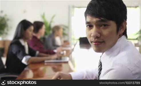 Young Asian man at work as manager in business meeting and smiling at camera. Rack focus