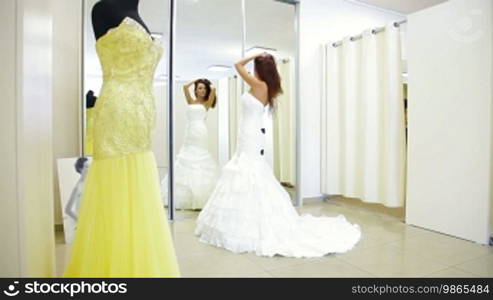 Young attractive woman choosing wedding dress in bridal boutique