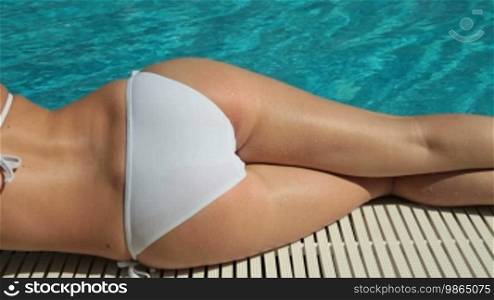 Young bikini woman sunbathing by swimming pool, rear view