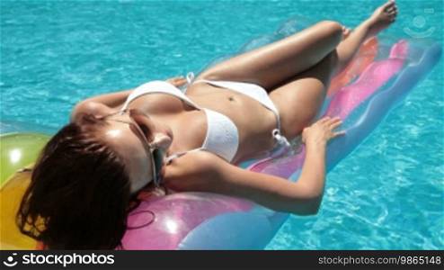 Young bikini woman sunbathing on a lilo in a swimming pool