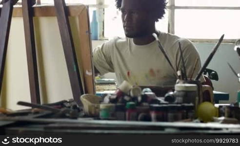 Young black people painting for hobbies. Proud African American man working as a professional painter, skillful Cuban artist in an art studio near a table full of equipment, tools, canvas, and paint