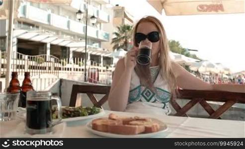 Young blond woman having a meal in an outdoor restaurant during summer holidays