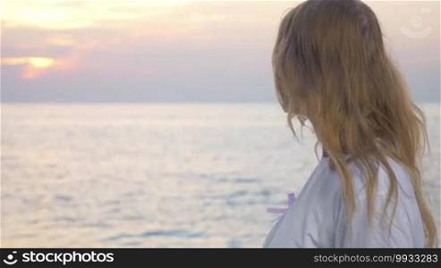 Young blond woman in white t-shirt wearing pink breast cancer awareness ribbon. She looking at the sea and then turning to camera. Support for people affected by cancer