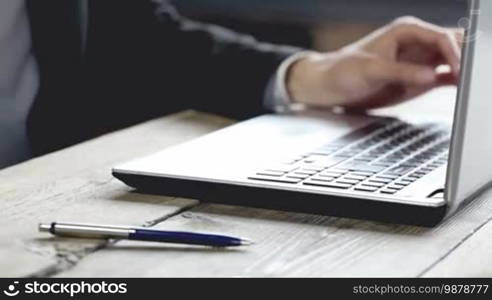 Young businessman in black suit using laptop in office