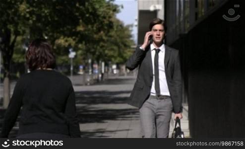 Young businessman talking on mobile phone and walking in the street. Slow motion