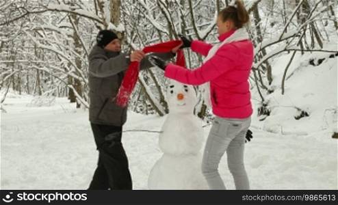 Young Couple Building Snowman In Winter Forest
