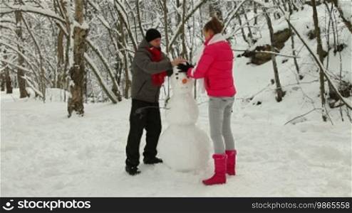 Young couple enjoying in a winter snowy forest, making a snowman